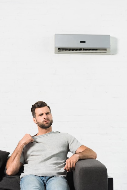 handsome-man-sitting-couch-suffering-from-heat-air-conditioner-home_824701-11869